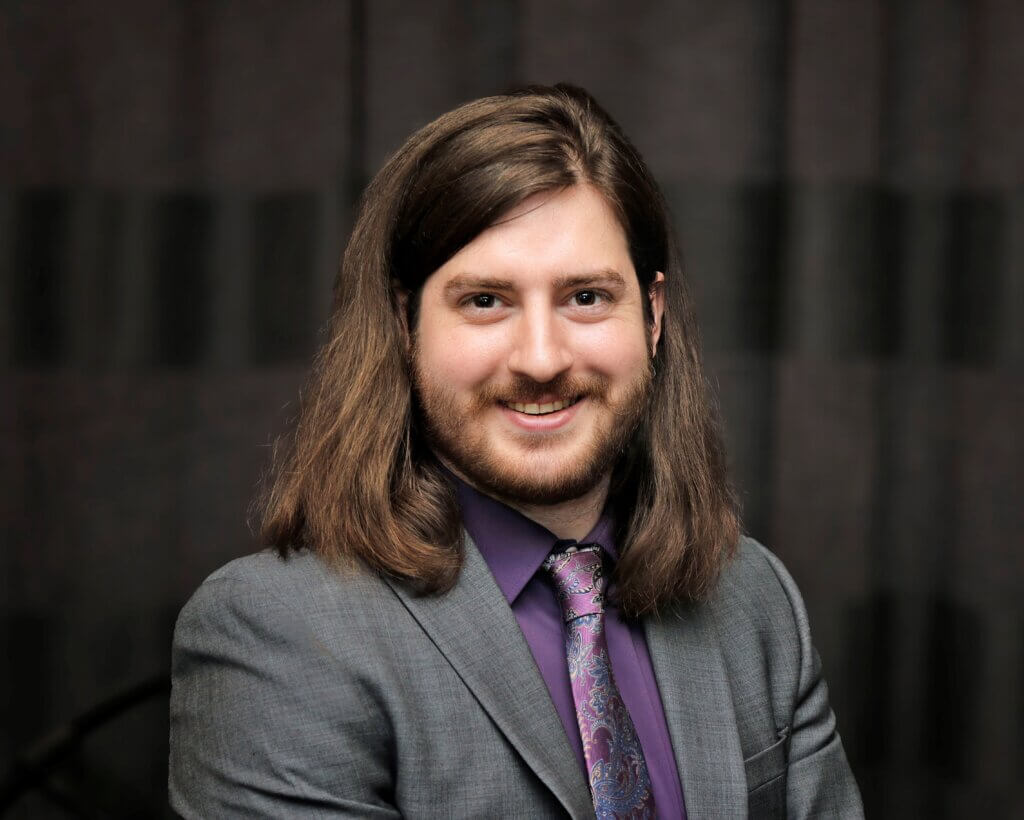 A smiling man with long, brown hair and neat facial hair