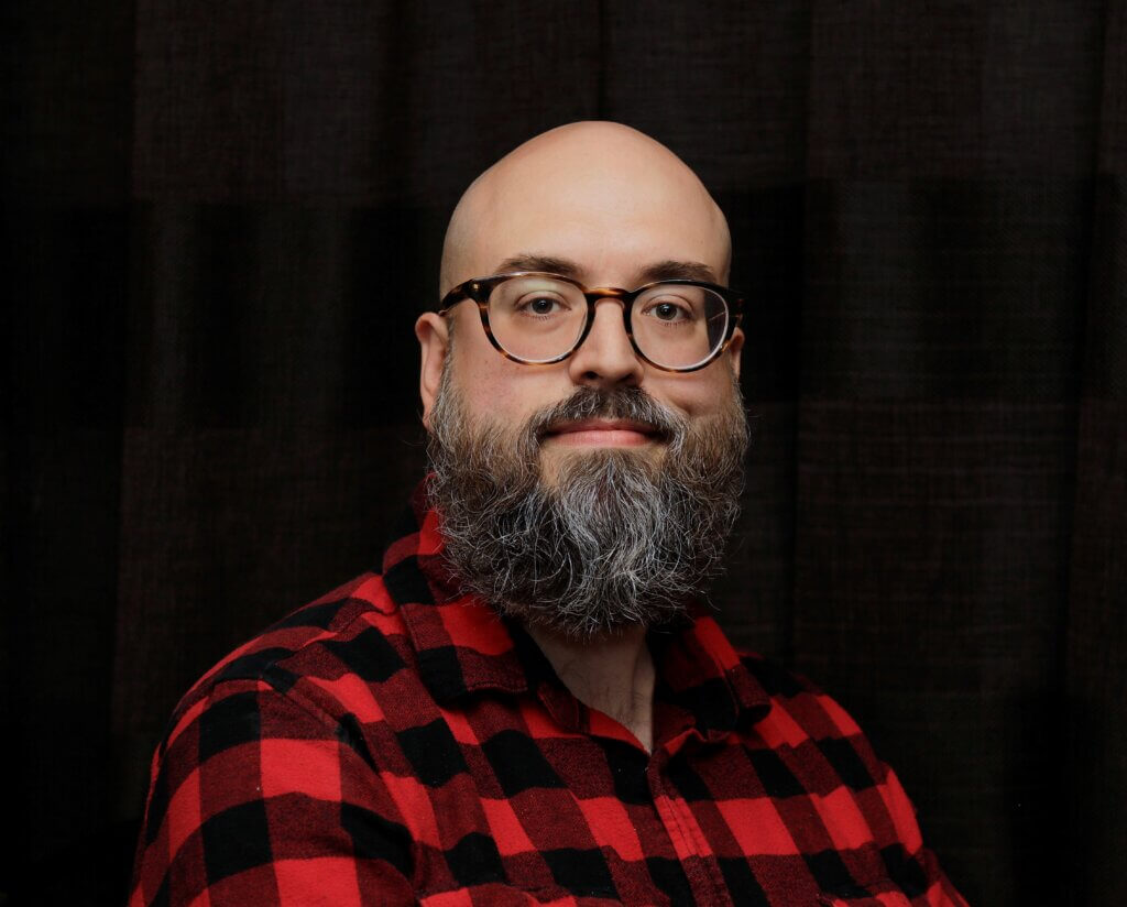 A smiling bald man with a beard wearing glasses