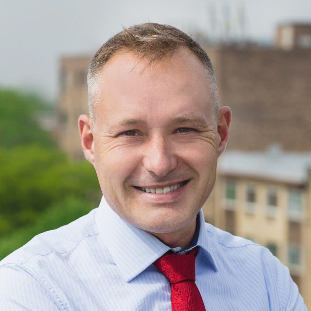 A smiling man with short hair wearing a tie