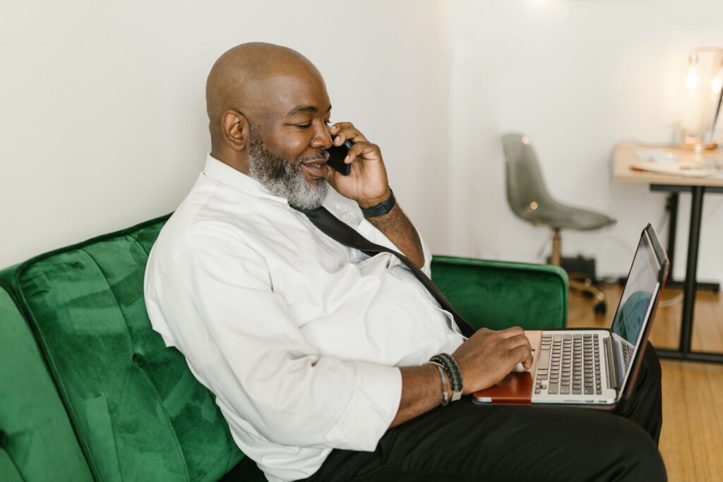 A businessperson sits on a couch with a laptop and talking on the phone